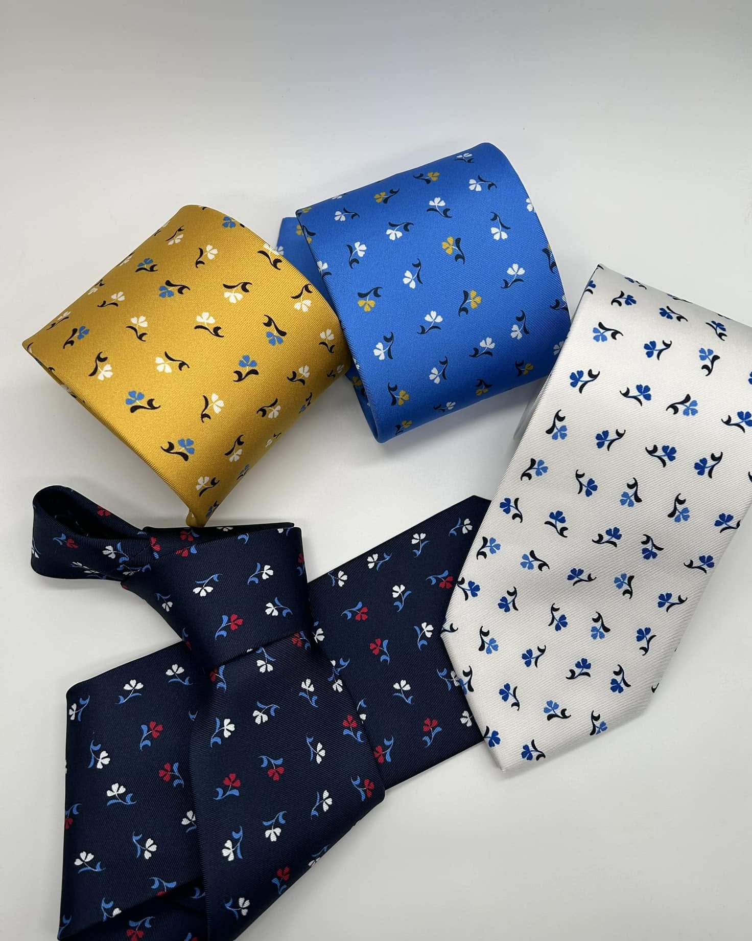Cravatte Salvatore Comella con piccoli motivi floreali su fondi giallo, azzurro, bianco e blu